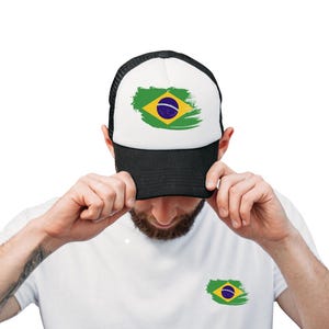 Peut inclure: Un chapeau de camionneur noir et blanc avec un motif de drapeau brésilien vert, jaune et bleu sur le devant. Le chapeau est tenu par une personne portant un t-shirt blanc avec un motif de drapeau brésilien plus petit sur le devant.