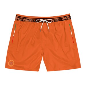 May include: Bright orange swim trunks with a black and gold geometric pattern on the waistband. The trunks have a white drawstring, side pockets with red, white, and green accents, and a gold emblem on the front. These shorts are perfect for a day at the beach or pool.
