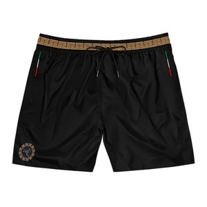 May include: Black swim trunks with a gold Greek key pattern waistband and a gold Greek key design on the left leg. The trunks have a red, white, and green Italian flag on the right side.
