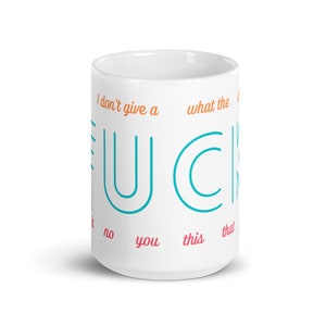 May include: White ceramic mug with the text "I don't give a" and "what the" in orange, and the word "F.U.C.K." in turquoise. The words "no", "you", "this", and "that" are written in pink.