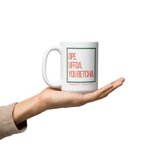 Peut inclure: Une tasse à café en céramique blanche avec une bordure verte et du texte rouge qui dit "OPE. UFFDA. YOU BETCHA. MIDWEST TRIFECTA"