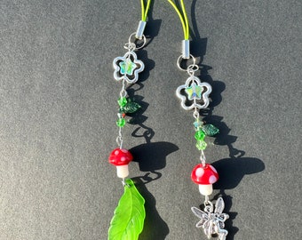 May include: Two green and silver charm phone straps with a mushroom, leaf, and flower charms. One strap also has a fairy charm.