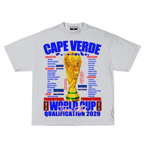 May include: A light gray t-shirt featuring the text "CAPE VERDE" in blue, with a gold trophy graphic. The shirt also lists team members and the text "WORLD CUP QUALIFICATION 2026".