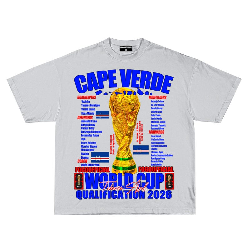 May include: A light gray t-shirt featuring the text "CAPE VERDE" in blue, with a gold trophy graphic. The shirt also lists team members and the text "WORLD CUP QUALIFICATION 2026".