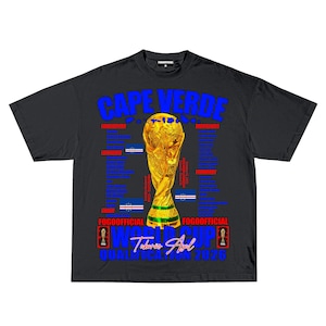 May include: Black t-shirt with a gold trophy graphic and the text "CAPE VERDE" in blue. The shirt also features the text "WORLD CUP" and "QUALIFICATION 2026". The shirt has a crew neck and short sleeves.