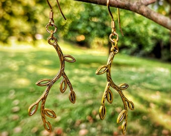 May include: Gold tone earrings with a delicate branch design featuring multiple leaves. The earrings are hanging from a tree branch.
