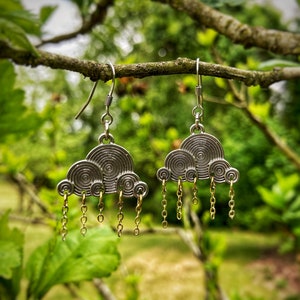 May include: Silver earrings shaped like clouds with dangling gold chains. The earrings are hanging from a tree branch.