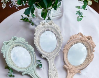 May include: Three ornate hand mirrors with pearl-like accents and floral designs. The mirrors have a light green, beige, and light pink finish.