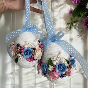 May include: Two white, fluffy Easter eggs decorated with blue and pink flowers and blue ribbon with white polka dots.