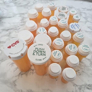 May include: A collection of orange prescription medicine bottles with white child-resistant caps. Some caps have printed instructions like "PUSH DOWN & TURN" and "HOLD TAB DOWN TURN". One bottle has the CVS logo.