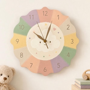 Può includere: Un orologio da parete con bordo smerlato e quadrante segmentato dai colori pastello con numeri marrone scuro da 1 a 12. Il centro presenta un'illustrazione di una nuvola sorridente color crema con piccole stelle e punti, e due lancette.