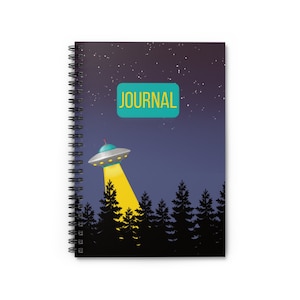 May include: A black spiral bound journal with a dark blue background and a starry night sky. A green rectangle with the word "JOURNAL" in yellow text is at the top of the page. A cartoon UFO with a yellow light beam is flying over a silhouette of a forest.