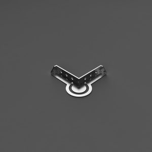 May include: A silver-coloured, V-shaped metal bracket with multiple screw holes. The bracket has a circular base with a concentric ring design. The object is set against a grey background.