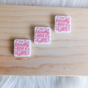 Peut inclure: Trois autocollants carrés blancs avec une inscription rose qui dit "Je suis littéralement juste une fille" avec des étoiles roses autour du texte.
