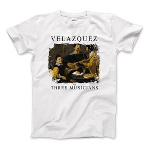 Puede incluir: Camiseta blanca con una imagen en blanco y negro de "VELAZQUEZ THE THREE MUSICIANS" impresa en la parte delantera.