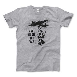 Puede incluir: Camiseta gris con una silueta negra de un avión que deja caer guitarras con el texto "Make Music Not War".