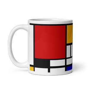 Könnte beinhalten: Weiße Keramiktasse mit einem geometrischen Design aus roten, gelben, schwarzen und blauen Quadraten.