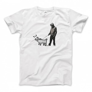 Puede incluir: Camiseta blanca con un gráfico en blanco y negro. El gráfico representa a una persona con una sudadera con capucha paseando a un perro con una correa. El perro es un contorno simple con una expresión de ladrido. La persona lleva una sudadera con capucha y pantalones oscuros.