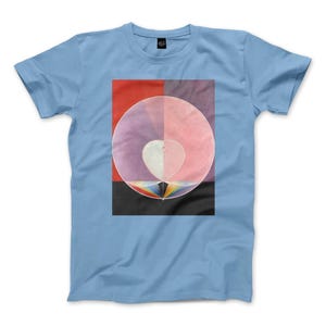 Puede incluir: Una camiseta de manga corta de color azul claro con un estampado gráfico central. El diseño muestra un círculo grande dividido en secciones rosa y morada, que contiene una forma de corazón blanco sobre un pequeño prisma arcoíris.