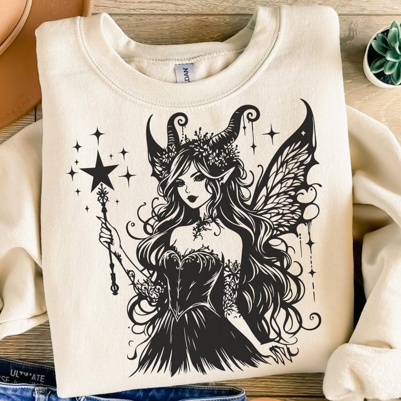 May include: Cream-colored sweatshirt featuring a black graphic of a fairy with long hair, wings, and a star-topped wand. The fairy is adorned with a crown and a dark dress. Stars and decorative lines surround the fairy.