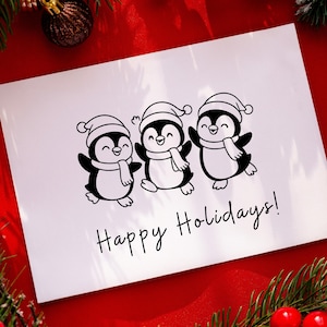 May include: A white greeting card with three cartoon penguins wearing Santa hats and scarves. The penguins are black and white with smiling faces. The words "Happy Holidays!" are written in black script below the penguins. The card is on a red surface.