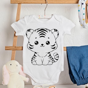 K&ouml;nnte beinhalten: Wei&szlig;er Baby-Body mit einem schwarz-wei&szlig;en Cartoon-Tiger-Design. Der Tiger hat gro&szlig;e Augen und Streifen. Der Body h&auml;ngt an einem Holzb&uuml;gel. Blaue Jeanshose und ein Stoffhase sind im Hintergrund.