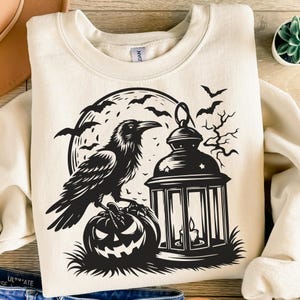 Pu&ograve; includere: Felpa color crema con un design nero a tema Halloween. La grafica include un corvo appollaiato su una zucca, una lanterna accesa, pipistrelli e una luna piena. Il design &egrave; centrato sul davanti.
