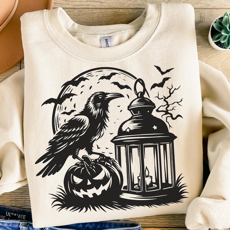 Pu&ograve; includere: Felpa color crema con un design nero a tema Halloween. La grafica include un corvo appollaiato su una zucca, una lanterna accesa, pipistrelli e una luna piena. Il design &egrave; centrato sul davanti.