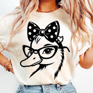 May include: A cream-colored t-shirt featuring a black and white graphic of a duck wearing glasses and a polka dot bow. The duck has detailed feathers and a stylish look. The design is centered on the shirt.