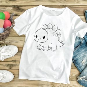 May include: White t-shirt featuring a black and white cartoon dinosaur illustration. The dinosaur has a friendly expression and is outlined in black. The shirt is made of a soft, comfortable material.