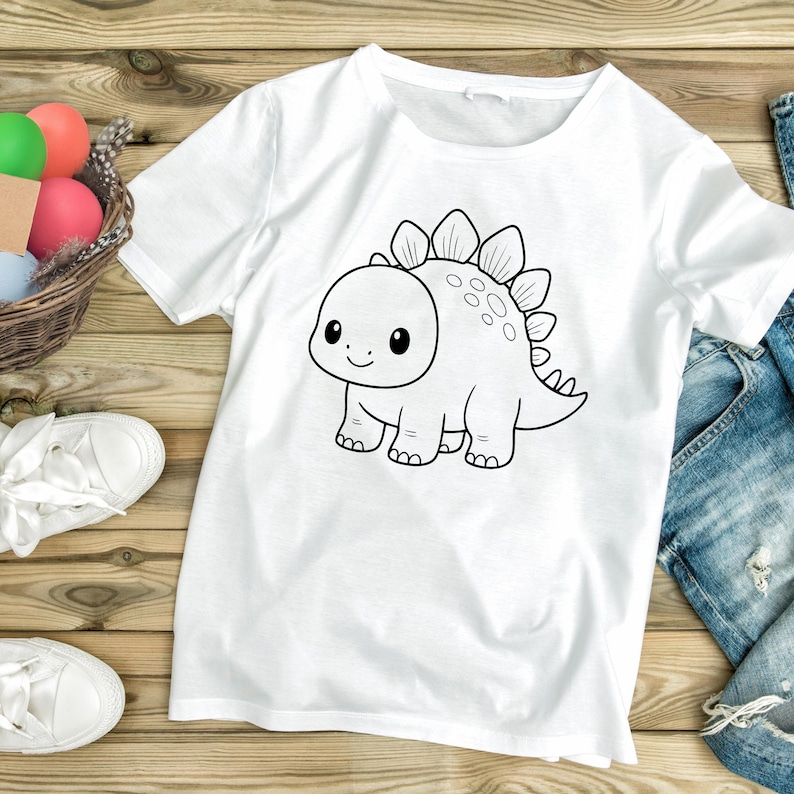 May include: White t-shirt featuring a black and white cartoon dinosaur illustration. The dinosaur has a friendly expression and is outlined in black. The shirt is made of a soft, comfortable material.