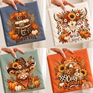 Könnte beinhalten: Vier gefaltete T-Shirts mit herbstlichen Motiven. Das blaue Shirt zeigt gestapelte Kürbisse mit Gürteln und den Text Howdy Fall. Das weiße Shirt zeigt einen Kuhschädel mit Blumen und den Text Wild at Heart. Das grüne Shirt zeigt ein Hochlandrind mit Hut, und das orangefarbene Shirt zeigt Pilze und Kürbisse mit dem Text Cozy Season.
