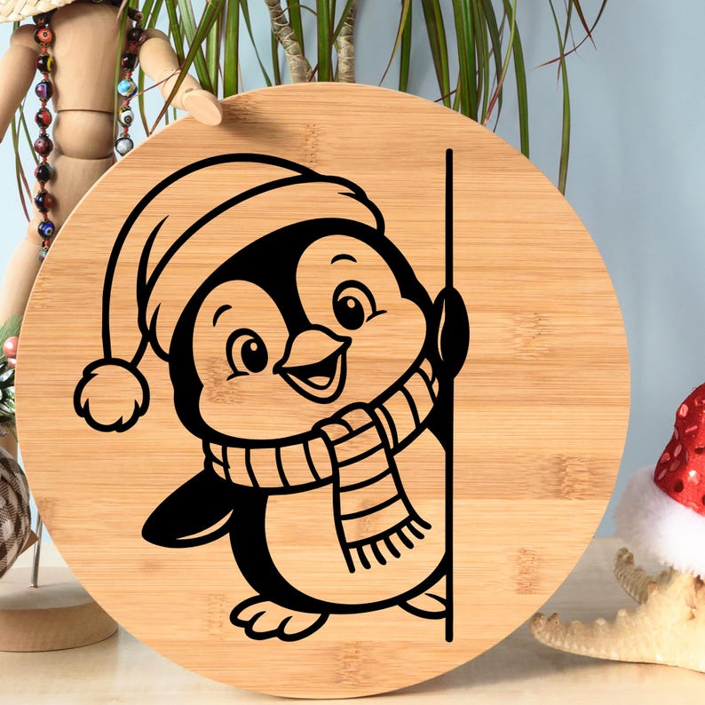 K&ouml;nnte beinhalten: Ein rundes Holzschneidebrett mit einem schwarzen Cartoon-Pinguin-Design. Der Pinguin tr&auml;gt eine M&uuml;tze und einen Schal. Das Brett hat ein hellbraunes Bambusmaserungsmuster.