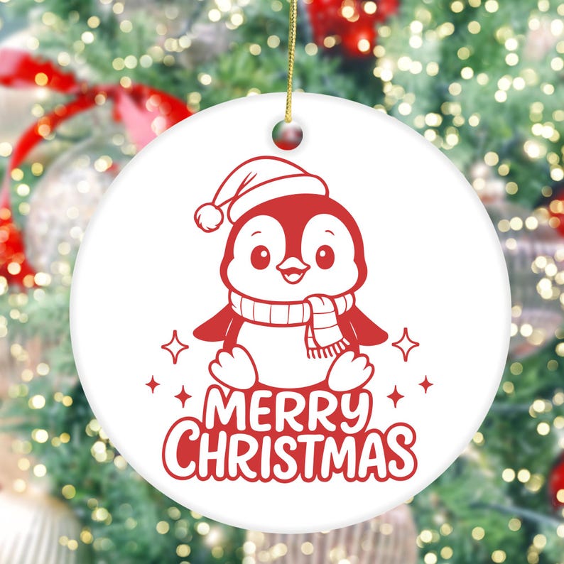 K&ouml;nnte beinhalten: Wei&szlig;er, runder Weihnachtsschmuck mit einem roten Pinguin, der einen Weihnachtsmannhut und einen Schal tr&auml;gt. Die Worte "MERRY CHRISTMAS" sind in roter Schrift unter dem Pinguin geschrieben. Der Schmuck hat eine goldene Schnur zum Aufh&auml;ngen.