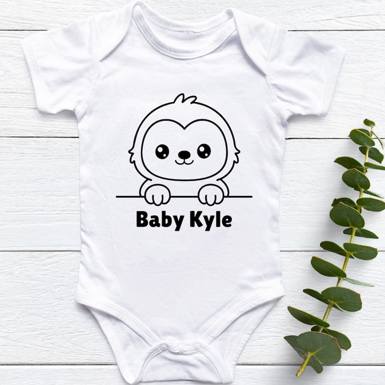 May include: White baby onesie with a black and white cartoon sloth graphic and the text "Baby Kyle". The onesie is short-sleeved and has a simple, clean design, perfect for a newborn or infant.