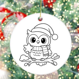 May include: A white ceramic Christmas ornament featuring a black and white cartoon owl wearing a Santa hat and scarf, holding a star. The owl is perched on a branch with snow. A gold string is attached for hanging.