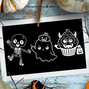 May include: A rectangular black sign featuring three white line art illustrations: a dancing skeleton wearing striped socks, a ghost with a small pumpkin on its head, and a cupcake character with horns holding a small pumpkin treat bag.