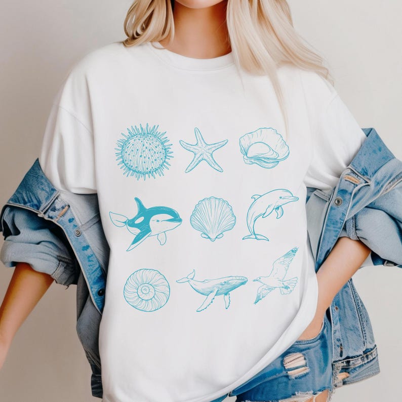 K&ouml;nnte beinhalten: Wei&szlig;es T-Shirt mit hellblauer Illustration verschiedener Meeresbewohner, darunter Seeigel, Seestern, Muschel, Orca, Delfin, Wal und M&ouml;we. Das Design ist eine einfache Strichzeichnung, ideal f&uuml;r Meeresliebhaber.