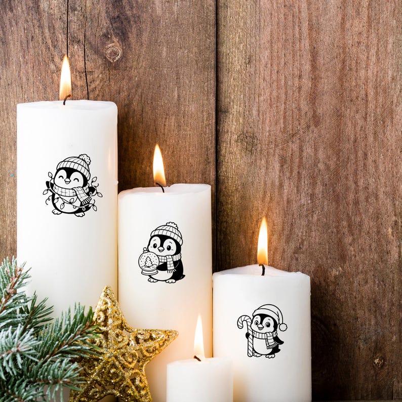 K&ouml;nnte beinhalten: Wei&szlig;e Stumpenkerzen mit schwarz-wei&szlig;en Pinguin-Designs, die warm leuchten. Ein goldener Stern und Tannenzweige tragen zum festlichen Feiertags-Thema bei. Die Kerzen stehen vor einem rustikalen Holz Hintergrund.