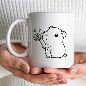 Puede incluir: Taza de cer&aacute;mica blanca con un dibujo de l&iacute;nea negra de un h&aacute;mster soplando sobre un diente de le&oacute;n. El h&aacute;mster tiene ojos grandes y una boca peque&ntilde;a.
