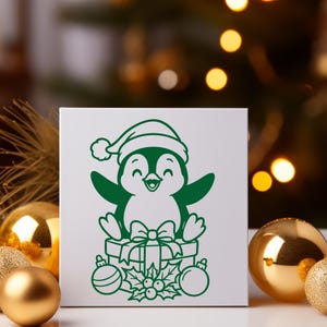 K&ouml;nnte beinhalten: Eine wei&szlig;e quadratische Karte zeigt einen gr&uuml;nen Cartoon-Pinguin mit Weihnachtsm&uuml;tze. Der Pinguin sitzt auf einer Geschenkbox mit Schleife, umgeben von Kugeln und Stechpalmen. Das Design ist festlich und f&uuml;r Weihnachten geeignet.