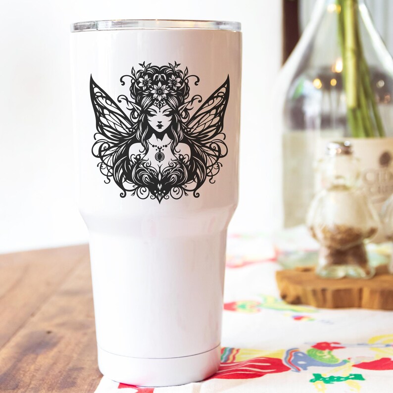 May include: White insulated tumbler featuring a black illustration of a fairy with detailed wings, a floral crown, and ornate jewelry. The design is centered on the tumbler, which has a silver rim and a white body.