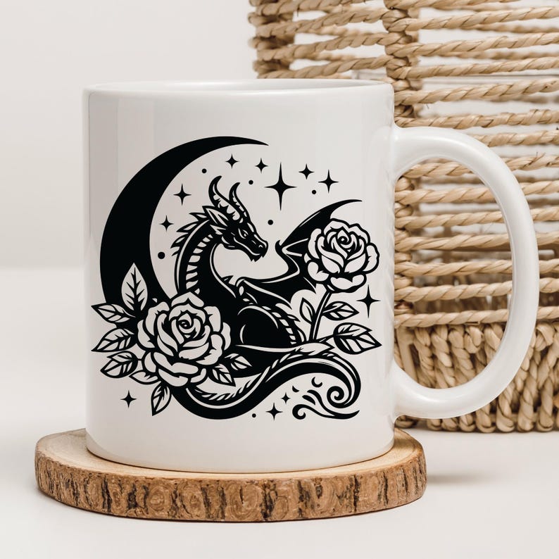 Puede incluir: Taza de cer&aacute;mica blanca con un dise&ntilde;o en blanco y negro de un drag&oacute;n enroscado alrededor de una luna creciente con rosas y estrellas.