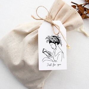 May include: A white gift tag with a black line drawing of a person reading a book with flowers in their hair. The text "Just for you" is printed on the tag.