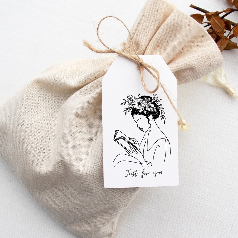 May include: A white gift tag with a black line drawing of a person reading a book with flowers in their hair. The text "Just for you" is printed on the tag.