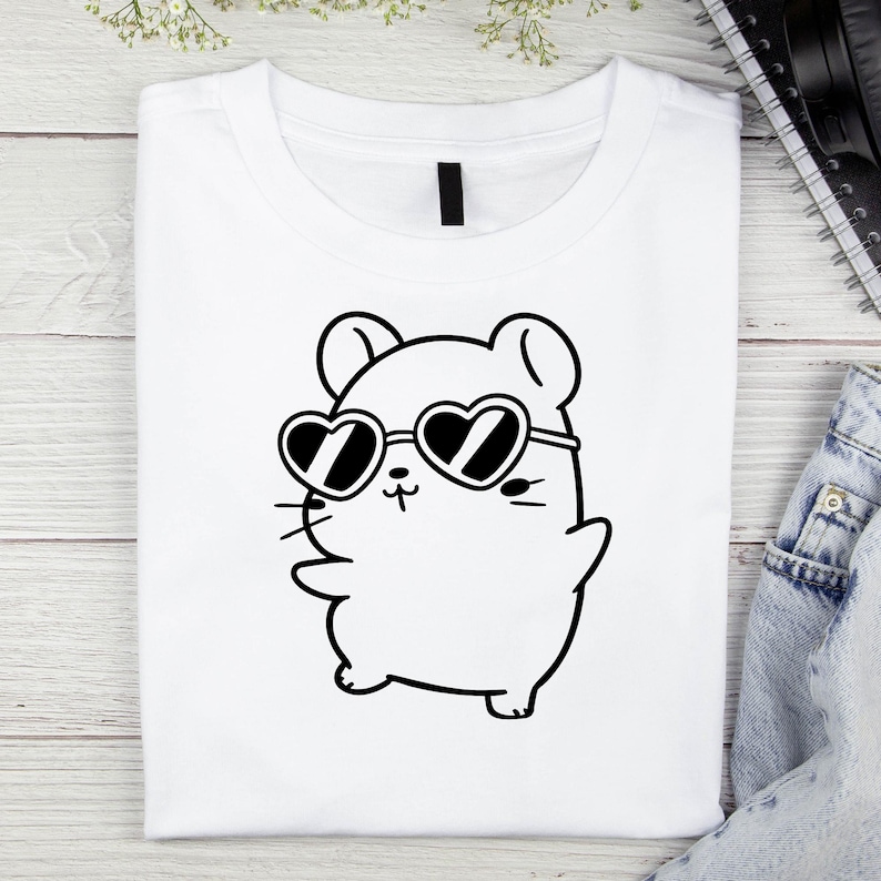 Puede incluir: Una camiseta blanca con un dibujo de l&iacute;nea negra de un h&aacute;mster de dibujos animados que lleva gafas en forma de coraz&oacute;n.