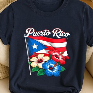 May include: Navy blue t-shirt with the words "Puerto Rico" above a design of the Puerto Rican flag and hibiscus flowers. The graphic uses red, white, blue, and yellow, creating a vibrant and patriotic design.