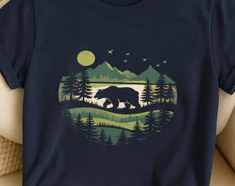 May include: Navy blue t-shirt featuring a nature scene with a bear silhouette walking across a landscape of green trees, hills, and mountains. A yellow moon and birds are in the sky. The design is contained within a circular shape.