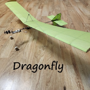 May include: A green and white model airplane with a propeller and wheels. The airplane is labeled "Dragonfly".