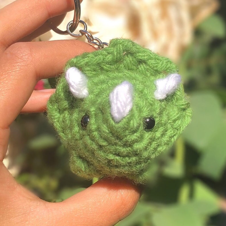 May include: Green crocheted triceratops keychain with white horns and black eyes.